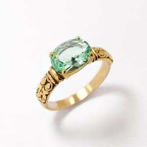 May include: A gold ring with an oval-shaped green gemstone set in a decorative band.