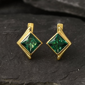 May include: A pair of gold earrings with square green gemstones. The earrings have a simple, modern design.