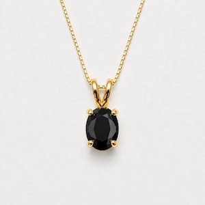 May include: A gold necklace featuring a delicate box chain and a pendant with a single oval-cut black gemstone held in a four-prong setting. The pendant is suspended from a gold bail that connects directly to the thin, polished gold chain.