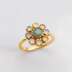 May include: A gold ring with a green gemstone surrounded by smaller white gemstones. The ring is set in a flower shape.