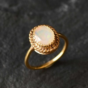 May include: A gold ring with a white opal gemstone set in a rope-like design.