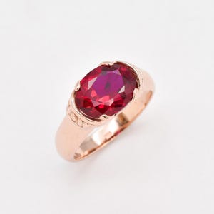 May include: A rose gold ring with a large, oval-shaped, red gemstone set in a decorative, ornate setting.