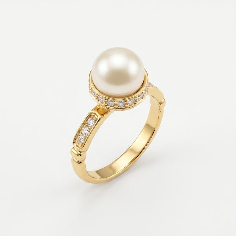 May include: A gold ring featuring a large, round, cream-colored pearl set in a halo of small, clear, sparkling stones. The band is crafted from polished yellow gold and includes a channel of three small, clear stones on each side of the setting.