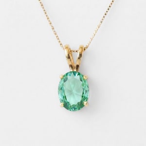 Puede incluir: Un collar de oro con un colgante de piedra preciosa de color verde claro y corte ovalado, sujeto por un engaste de cuatro garras. El colgante cuelga de una delicada cadena de oro conectada a la parte superior mediante una anilla.