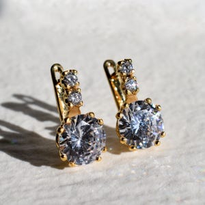 May include: A pair of gold hoop earrings with a large clear round stone and three smaller clear stones on the top of each hoop.