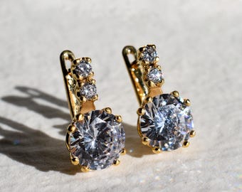May include: A pair of gold hoop earrings with a large clear round stone and three smaller clear stones on the top of each hoop.