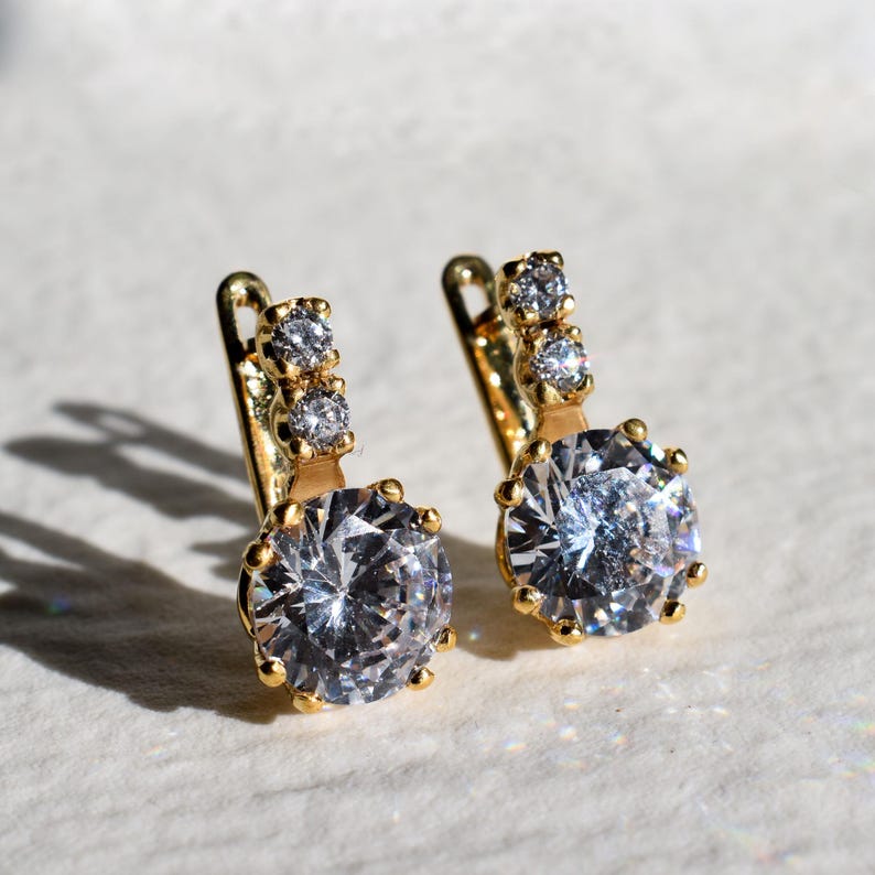 May include: A pair of gold hoop earrings with a large clear round stone and three smaller clear stones on the top of each hoop.