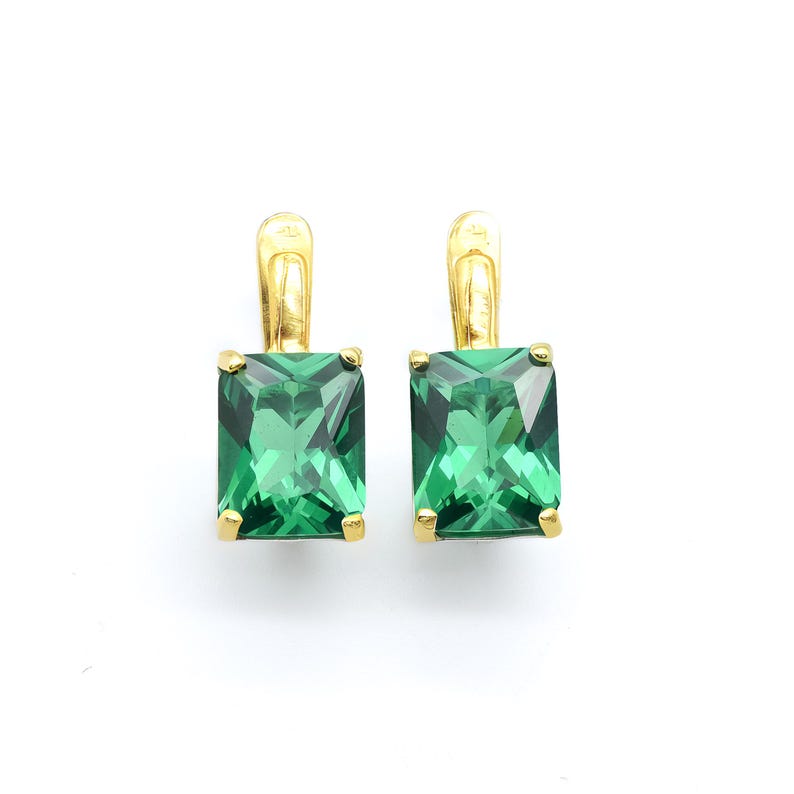 Pode incluir: Um par de brincos de ouro com pedras preciosas quadradas de cor verde esmeralda. Os brincos t&ecirc;m um design simples e elegante.