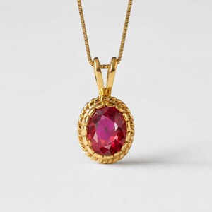 May include: A gold pendant necklace featuring an oval-shaped, faceted deep pink gemstone set within a twisted rope-style gold border. The pendant hangs from a delicate gold box chain, showcasing a polished metal finish and a vibrant, clear stone.