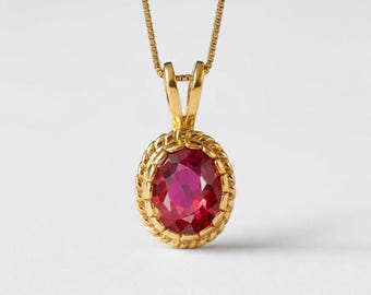 Könnte beinhalten: Eine goldene Anhängerkette mit einem ovalen, facettierten, tiefrosa Edelstein, der in eine gedrehte, seilartige Goldfassung eingefasst ist. Der Anhänger hängt an einer zarten Goldkette und zeigt eine polierte Metalloberfläche.