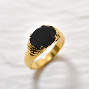 May include: A gold ring with a large oval-shaped black gemstone. The ring has a detailed design around the gemstone.