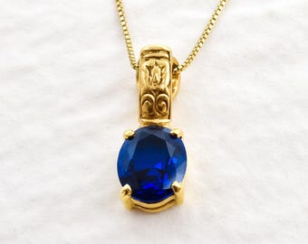 May include: A gold chain necklace with a blue gemstone pendant. The pendant has an ornate gold design around the gemstone.