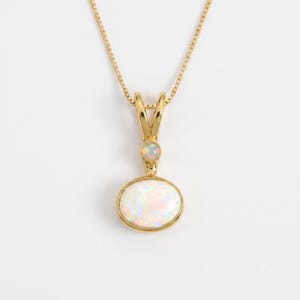 May include: A gold necklace featuring a pendant with a large oval opal and a smaller round opal set above it. The pendant is suspended from a delicate gold box chain. The opals display iridescent flashes of color against a polished gold setting.