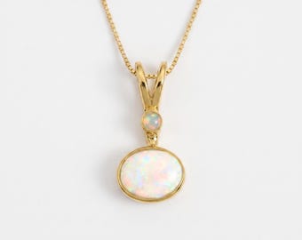 May include: A gold necklace featuring a pendant with a large oval opal and a smaller round opal set above it. The pendant is suspended from a delicate gold box chain. The opals display iridescent flashes of color against a polished gold setting.