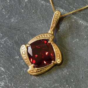 May include: A gold pendant necklace with a large, square, red gemstone set in a gold frame. The frame has a detailed, ornate design.
