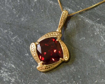 May include: A gold pendant necklace with a large, square, red gemstone set in a gold frame. The frame has a detailed, ornate design.