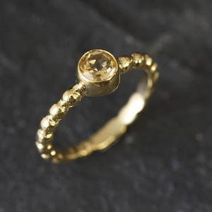May include: A gold ring with a beaded band and a single round, light yellow gemstone.