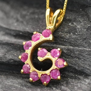 Può includere: Una collana con ciondolo in oro a forma di spirale con rubini rosa.