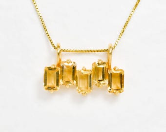 Op de afbeelding: Een gouden ketting met een hanger met vijf rechthoekige, gefacetteerde, gele edelstenen.