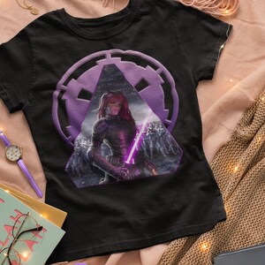 May include: Black t-shirt with a purple and white graphic of a female character holding a lightsaber in front of a group of soldiers. The graphic is set inside a purple triangle with a circle behind it.