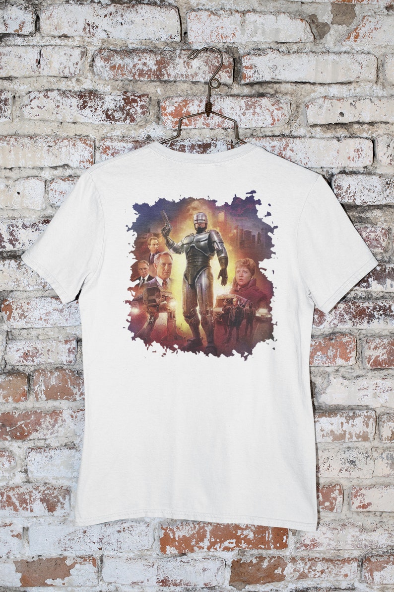 May include: White t-shirt with a graphic print of a silver robot character from the movie Robocop. The robot is standing in front of a cityscape with other characters in the background.