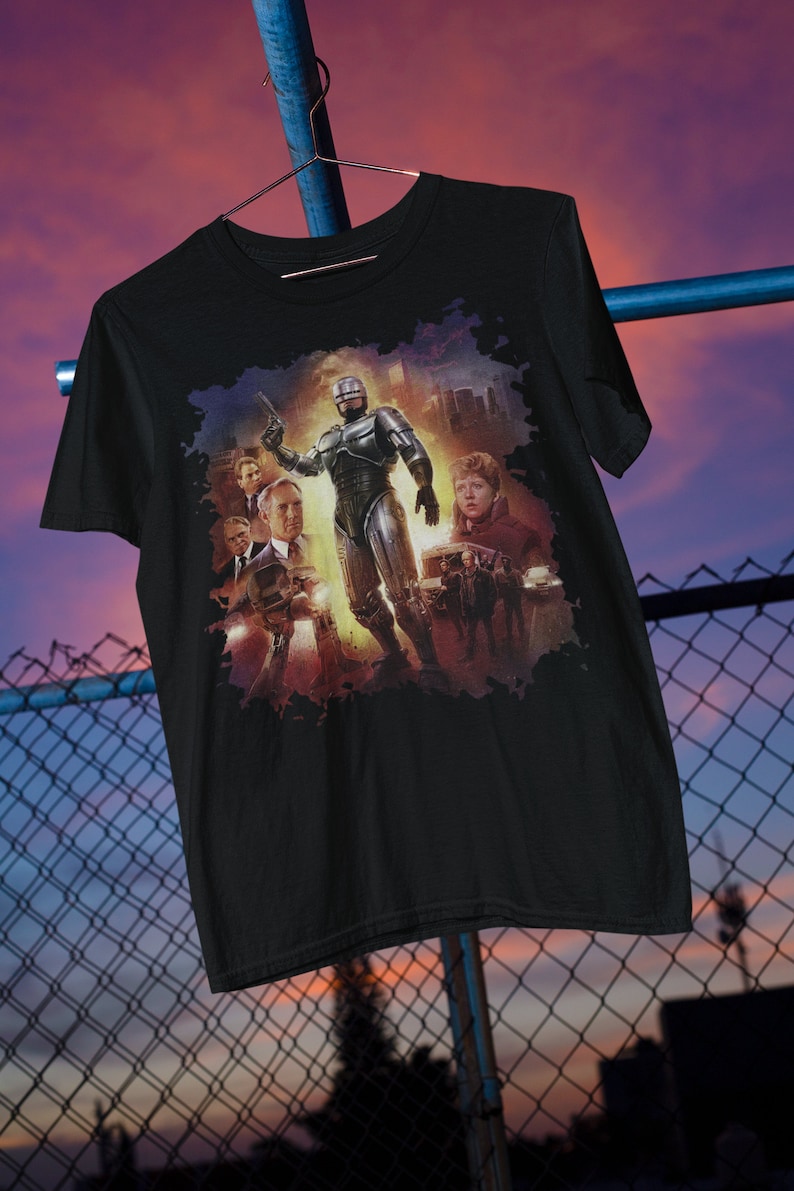 May include: Black t-shirt with a graphic print of the Robocop movie characters. The graphic features Robocop in the center with other characters from the movie surrounding him.