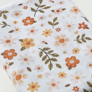 Op de afbeelding: Witte stof met een bloemenpatroon met oranje, gele en groene bloemen. De stof is dubbelgevouwen.