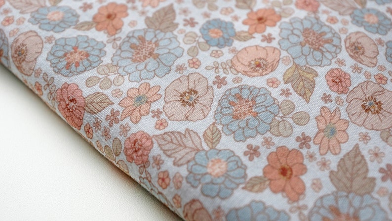 May include: A light blue fabric with a floral pattern in shades of pink and brown. The fabric features a variety of flowers, including roses, daisies, and poppies.