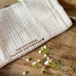 May include: A white muslin baby blanket with the embroidered text "Trust your instincts. You know your baby best." and a small heart.