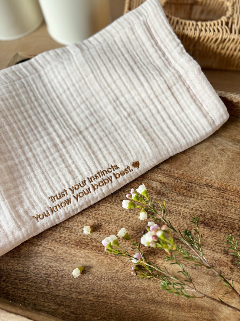 May include: A white muslin baby blanket with the embroidered text "Trust your instincts. You know your baby best." and a small heart.