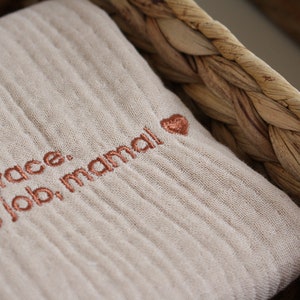 May include: A beige muslin fabric square with the text "Self grace. Amazing job, mama!" embroidered in copper-colored thread with a small heart.
