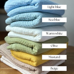 May include: A stack of seven folded fabric swatches in various colors, including light blue, sea blue, warm white, olive, mustard, beige, and cream. The swatches are arranged from lightest to darkest.