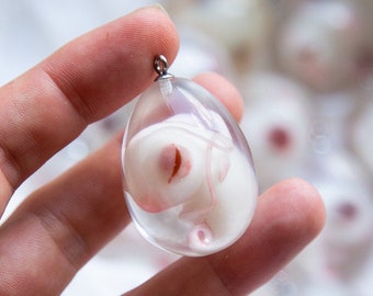 May include: A small, white, resin animal figurine encased in a clear, round, resin pendant. The pendant is hanging from a silver chain.