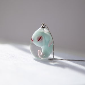 May include: A silver chain necklace with a clear glass pendant containing a small blue and white figurine with red eyes.