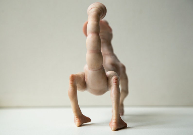 May include: A nude-colored ceramic sculpture of a creature with a long, segmented tail and four legs. The creature is standing on a white surface.