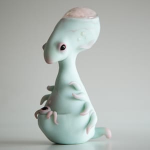 May include: A whimsical, light-blue alien sculpture with pink accents. The creature has large eyes, a bulbous head, and multiple tentacles. The sculpture appears to be made of ceramic or a similar material, with a smooth, glossy finish.