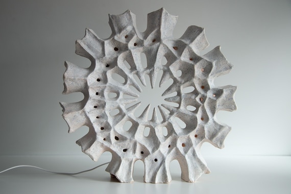 A hand-thrown ceramic lamp sculpted into the Wheel of Samsara — organic, cave-like ambient light that looks like it belongs in a museum not a marketplace.