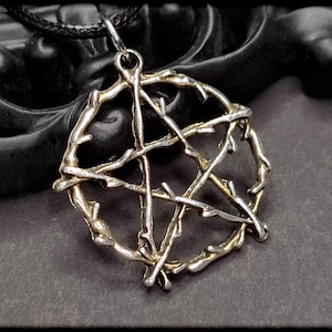 May include: A silver pendant necklace with a pentagram design made of intertwined branches. The pendant is on a black cord.