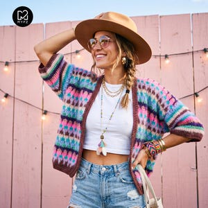 Peut inclure: Un gilet en crochet multicolore avec des rayures horizontales dans des tons de rose, bleu, violet et marron. Le vêtement est porté sur un haut court blanc uni et un short en jean bleu clair, accompagné d'un chapeau fedora beige et de colliers.