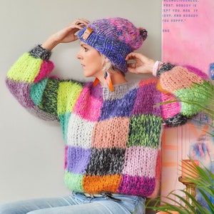 May include: A colorful patchwork knit sweater with a multi-colored knit hat. The sweater has a variety of colors including pink, purple, green, yellow, and orange. The hat has a pom-pom on top.