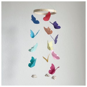 May include: A colorful felt butterfly mobile with a wooden ring. The butterflies are in shades of blue, red, orange, yellow, green, and purple. The mobile is hanging from a white ceiling.