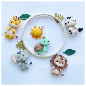 Op de afbeelding: Een houten ringmobile met vilt dieren en zon uitsparingen. De mobile heeft een gele giraffe, een groene schildpad, een bruine leeuw, een grijze olifant en een wit zebra. De zon is geel met een glimlachend gezicht.