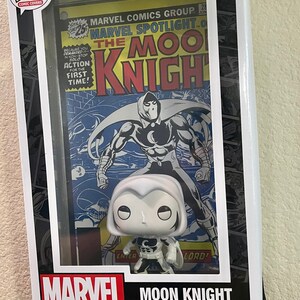 May include: A white Moon Knight Funko Pop! Comic Covers figure in a clear plastic display case with a vintage Marvel Spotlight comic book featuring Moon Knight. The comic book cover features the text "Marvel Spotlight" and "The Moon Knight".