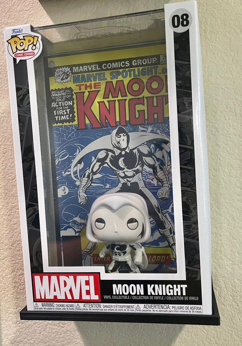 May include: A white Moon Knight Funko Pop! Comic Covers figure in a clear plastic display case with a vintage Marvel Spotlight comic book featuring Moon Knight. The comic book cover features the text "Marvel Spotlight" and "The Moon Knight".
