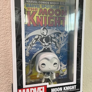 May include: A Funko Pop! Comic Covers vinyl collectible figure of Moon Knight in a black and white costume. The figure is displayed in a clear plastic case with a vintage Marvel Spotlight comic book featuring Moon Knight on the cover. The comic book cover is yellowed and has a red title.