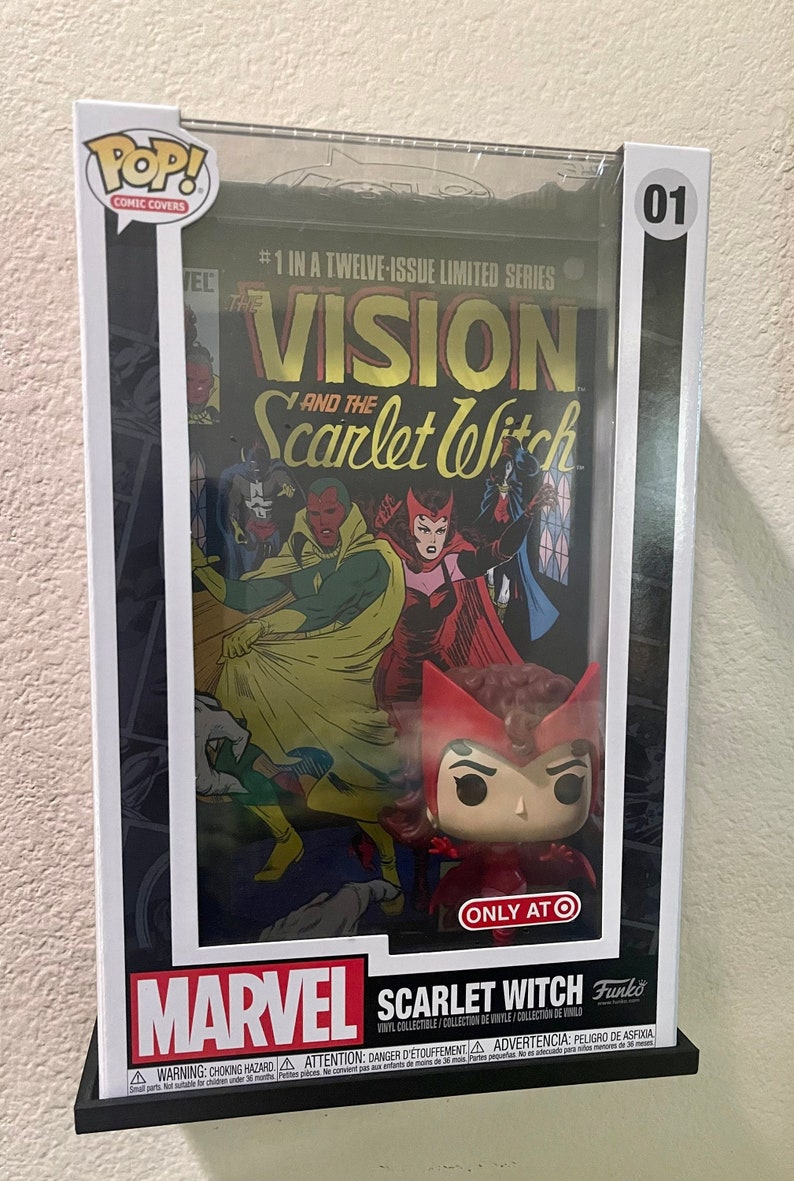 May include: A clear plastic display case with a red and yellow comic book featuring the Vision and the Scarlet Witch. The case also contains a Funko Pop! vinyl figure of the Scarlet Witch. The case has a white background with black text that reads "#1 in a twelve-issue limited series" and "The Vision and the Scarlet Witch". The case also has a white label with black text that reads "Marvel Scarlet Witch Vinyl Collectible/Collection de Vinyle/Collection de Vinilo".