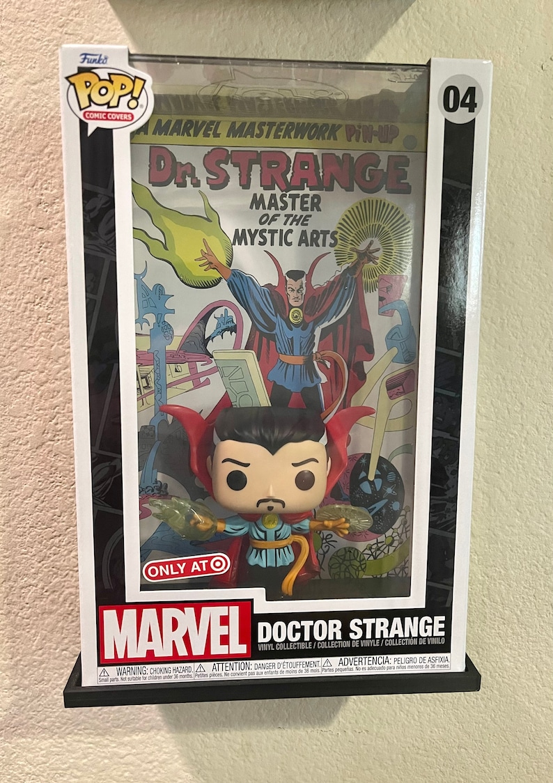 May include: A Funko Pop! Comic Covers collectible figure of Doctor Strange, the Master of the Mystic Arts, in a clear plastic display case with a vintage comic book cover featuring Doctor Strange. The case has a black and white border and a white background with the number 04 in the top right corner. The comic book cover features a yellow and orange flame effect and the text "Marvel Masterwork Pin-Up Dr. Strange Master of the Mystic Arts". The figure is wearing a red cape and a blue and yellow costume. The figure is holding a green and yellow energy ball in each hand. The case has a white label on the bottom with the text "Marvel Doctor Strange Vinyl Collectible/Collection de Vinyle/Colecci&oacute;n de Vinilo" and a warning label with the text "WARNING: CHOKING HAZARD ATTENTION: DANGER D'ETOUFFEMENT ADVERTENCIA: PELIGRO DE ASFIXIA".
