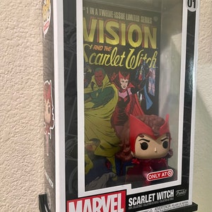 May include: A white and black Pop! Comic Covers collectible figure of Scarlet Witch from Marvel Comics. The figure is in a clear plastic display case with a black base. The figure is holding a red cape and has a red and white costume. The figure is standing in front of a comic book cover featuring Vision and Scarlet Witch. The comic book cover is titled "Vision and the Scarlet Witch." The comic book cover is number 1 in a 12-issue limited series.
