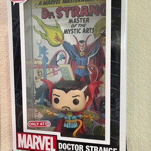 May include: A Funko Pop! Comic Covers collectible figure of Doctor Strange in a red and blue costume, holding a glowing green orb. The figure is displayed in a clear plastic case with a vintage comic book cover featuring Doctor Strange in a similar pose. The comic book cover is titled "Dr. Strange, Master of the Mystic Arts".