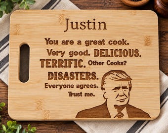 May include: A rectangular bamboo cutting board with a handle cutout on the left side. The board features laser-engraved text that reads: Justin, You are a great cook. Very good. DELICIOUS. TERRIFIC. Other Cooks? DISASTERS. Everyone agrees. Trust me.